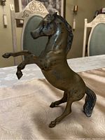 Brass horse figurine shown in profile on a patterned tablecloth, highlighting its rearing pose and metallic finish.