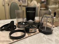 Photo of three Nutribullet cups, three blending lids with blades, three caps, and one screw-on lid placed on a table.