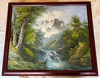 Full view of the framed oil painting showing a nature scene with river, trees, and mountains in the background.