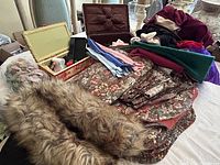 Overview of sewing lot showing two sewing kit boxes, fabric remnants including floral fabric, faux fur, assorted color fabric pieces and long zippers.