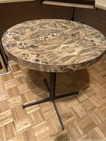Photo of a small round table with a metal pedestal base and a wood grain top showing signs of wear and needing refinishing.