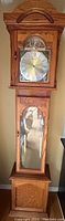 Full view of tall grandfather clock showcasing wooden case with glass door on bottom section and clock face with swinging pendulum above.
