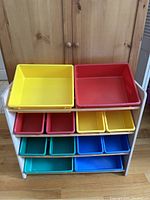 Frontal view of wooden toy organizer with 12 plastic bins in different colors on shelves