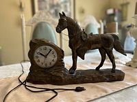 Full view of the vintage motorized clock lot showing the metal horse sculpture and the electric cord plug.