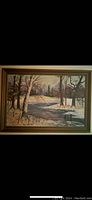 Full view of framed oil painting showing nature scene with trees and a river in autumn or early winter.