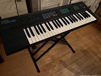 Full view of Yamaha PSR-16 keyboard resting on a black X-style stand on wooden floor.