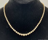 Graduated string of pearls displayed on a black bust, shows overall necklace form and size.