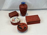 Overall grouping of five cinnabar carved items including ceramic lidded box and carved dragon motif vase with blue interior and brass rim.
