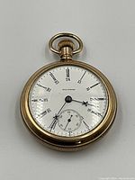 Front view of the gold plated pocket watch showing white dial with Roman numerals and a seconds subdial.