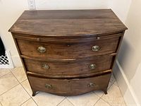 Front view showing bowed top, three drawers with brass hardware and bracket feet