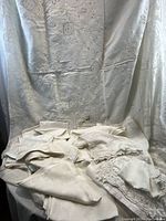 Assorted folded white linens displayed on a large embroidered tablecloth backdrop