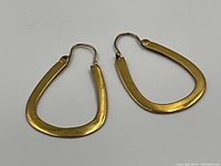 Pair of trapezoidal gold hoop earrings on white background, overhead view.