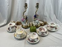Full view showing the pair of vintage lamps with porcelain couples and five assorted floral cups and saucers displayed in front