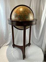 Front view of globe mounted on three-legged mahogany stand with full meridian and castors