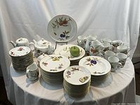 Wide view of entire porcelain set including stacks of plates, cups, teapot, coffee pot, creamer, sugar bowl on table.