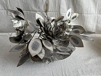 Front angle of vintage brutalist metal centerpiece showing flower and leaf design on textured base.