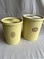 Front view of two butter yellow vintage Tupperware canisters with distinctive logos and lids, showing condition and size comparison.