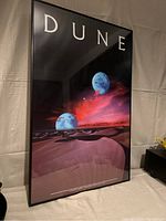 Front view of the Dune movie poster in black frame, showing the desert landscape and planets with red sky, framed under plexiglass.