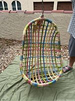 Front view of oval-shaped hanging chair covered in colorful macrame, hanging outdoors.