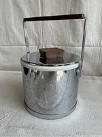 Front view of the vintage Kromex metal ice bucket showing wooden handle and lid knob. Reflective metal exterior with visible pitting and rust spots.