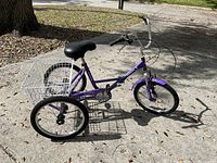 Full view of purple folding tricycle with rear storage basket set outdoors on pavement.