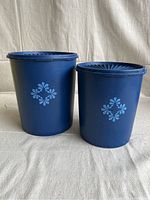 Front view of two royal blue Tupperware canisters with light blue floral pattern on front, standing side by side.