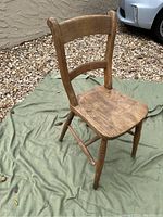 Left and front angle view of rustic wooden chair on green cloth, showing wood grain and damaged leg.