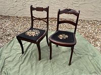 Front view showing two antique wooden chairs with embroidered floral seats and curved carved backs