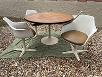 Full view of round tulip dining table with wooden top and four white swivel armchairs with brown cushions, showing overall condition and setup