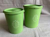Photo showing two lime green Tupperware canisters with white floral swirl designs on sides and fitted lids with sunburst pattern on top. The canisters are cylindrical in shape.