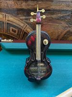 Front view showing detailed cello body shape, strings, tuning pegs, and broken tip area