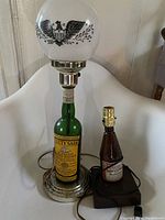 Two beer bottle lamps, one Cutty Sark whisky bottle with frosted globe and metal base, one Budweiser beer bottle with brass socket on wooden base