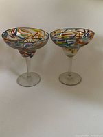 Two glass margarita glasses showing the colorful confetti dash pattern around the bowl and clear stems.