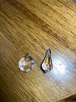 Two clear crystal pendants on wooden surface, one round and one teardrop shaped, each with metal bails.
