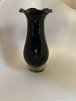 Full view of the black glass vase showing its flared wavy rim and clear ribbed glass base.