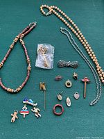 Full view of assorted costume jewelry items arranged on green surface showing necklaces, pins, brooches, rings, and charms.