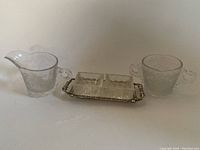 Full view of etched glass sugar bowl and creamer jug on either side of silver tray holding two glass salt and pepper shakers