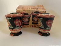 Front view of two floral hand painted ceramic salt and pepper shakers with original box behind.