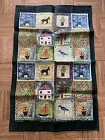 Front view of the Irish linen cloth laid flat showing its grid of colorful, folk-art style illustrations with various nature and home motifs.