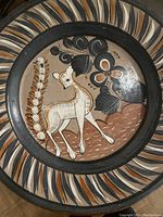 Close-up of round ceramic pottery plate with hand-painted deer and floral patterns in earthy tones and black.