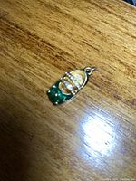 Close-up photo of the gold-tone shoe pendant on a wood surface showing the detailed rhinestones and loop for attachment.