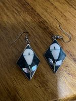 Front view of the pair of diamond-shaped cloisonné sterling silver earrings showing white flower design on black enamel background with iridescent accents.