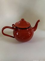 Photo of small vintage red enameled tea pot showing its rounded shape, curved spout, and handle with a lid topped by a knob.