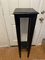 Front view of the black wood stand showing the square top, four legs, and lower shelf with scratches and wear marks.