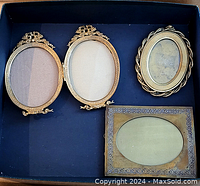 Set of four brass picture frames in a box showing their front sides, various shapes and decorative details.