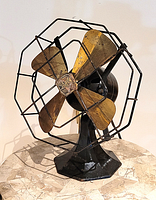 Front perspective showing brass blades, wire cage, and octagonal cast iron base.