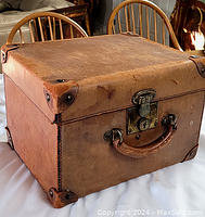Angled view of antique leather case showing top, side, leather handle, and reinforced corners.