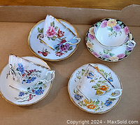 Four bone china teacups and saucers set with floral pattern and gold trim displayed in cardboard box.