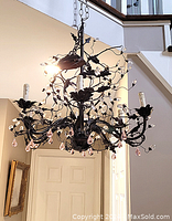 Full view of black metal chandelier hanging in a stairwell, showing the intricate metalwork and pink crystal pendants.