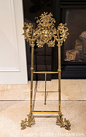 Full front view of brass easel unfolded showing overall height and structure in front of fireplace